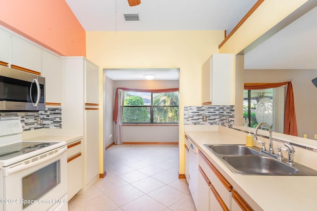 kitchen with tasteful backsplash, white appliances, sink, light tile patterned floors, and white cabinets