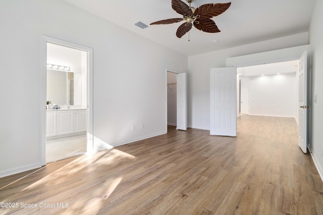 unfurnished bedroom with ensuite bathroom, a walk in closet, ceiling fan, light wood-type flooring, and a closet