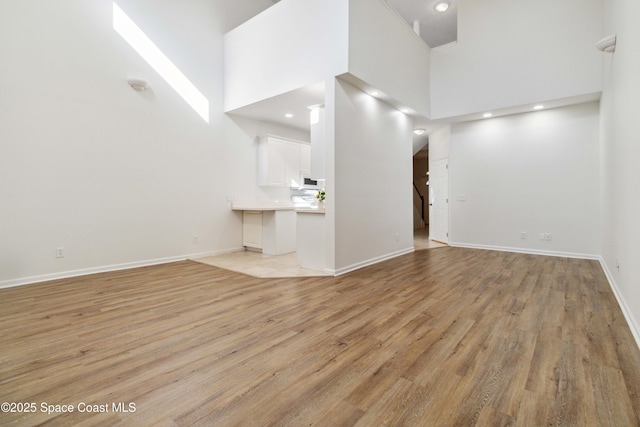 unfurnished living room featuring a high ceiling and light hardwood / wood-style flooring