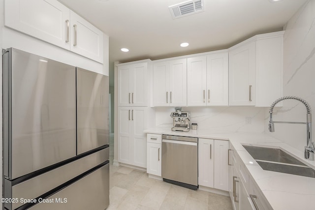 kitchen featuring sink, light stone counters, appliances with stainless steel finishes, white cabinets, and backsplash