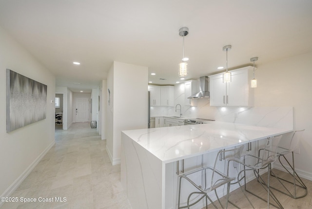 kitchen featuring white cabinetry, wall chimney exhaust hood, decorative light fixtures, and kitchen peninsula