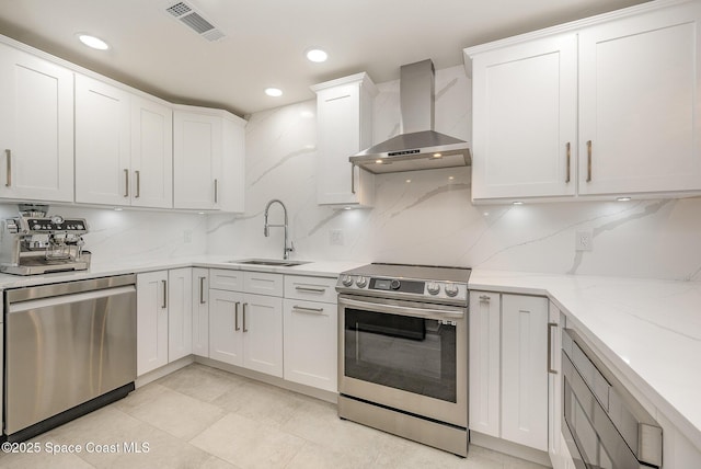 kitchen featuring sink, appliances with stainless steel finishes, white cabinetry, decorative backsplash, and wall chimney exhaust hood