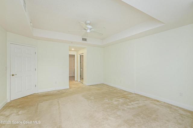 spare room featuring ceiling fan, a raised ceiling, and light carpet