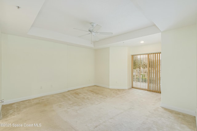 carpeted spare room with ceiling fan and a tray ceiling