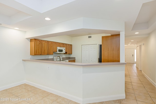 kitchen with stove, kitchen peninsula, light tile patterned floors, and stainless steel refrigerator