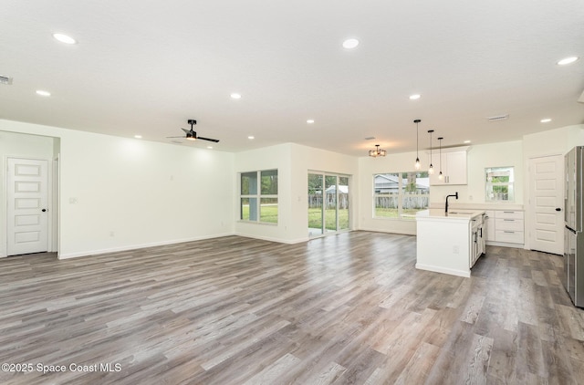 kitchen with sink, white cabinetry, light hardwood / wood-style flooring, an island with sink, and pendant lighting