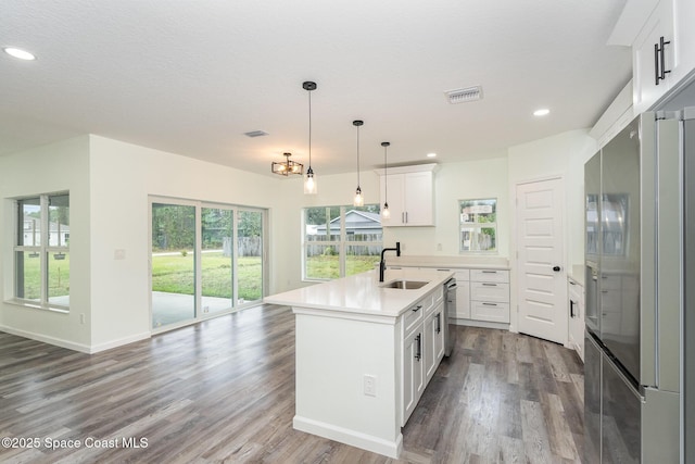 kitchen with pendant lighting, stainless steel refrigerator, white cabinetry, wood-type flooring, and a center island with sink