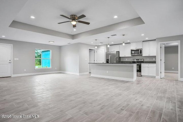 unfurnished living room with a raised ceiling, ceiling fan, and light hardwood / wood-style flooring