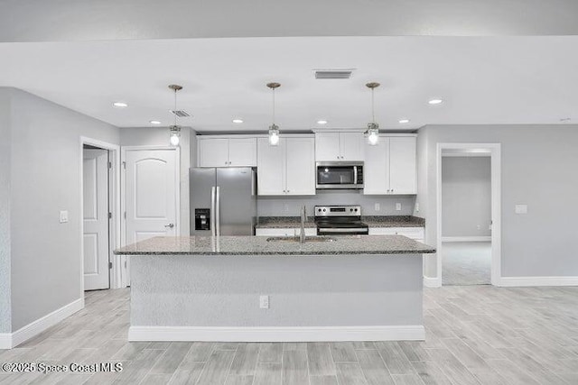 kitchen with white cabinetry, hanging light fixtures, stainless steel appliances, dark stone counters, and a center island with sink