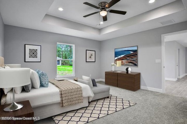 bedroom featuring a raised ceiling, ceiling fan, and light carpet