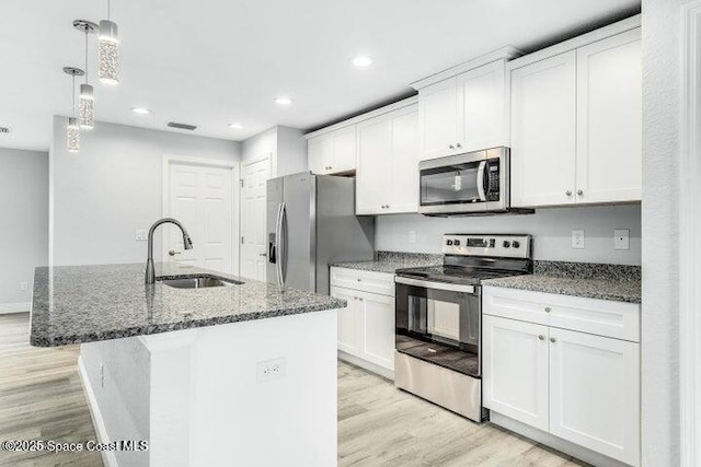 kitchen featuring white cabinetry, sink, stainless steel appliances, an island with sink, and decorative light fixtures