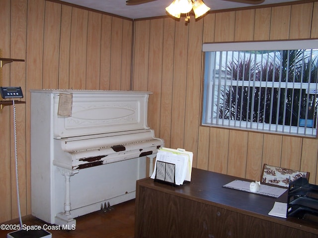 home office with ceiling fan and wood walls