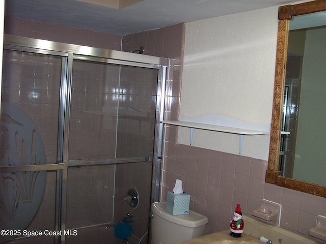 bathroom with toilet, a shower with shower door, and tile walls