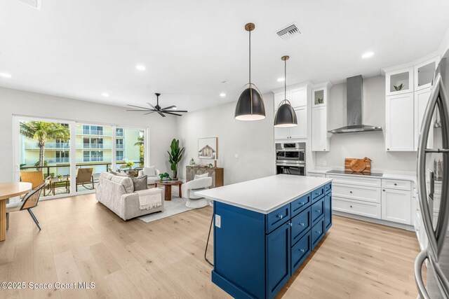 kitchen with decorative light fixtures, wall chimney range hood, blue cabinetry, and white cabinetry