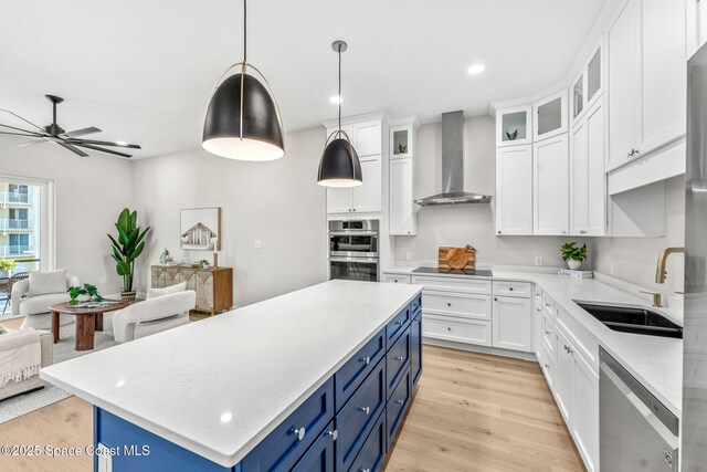 kitchen featuring a center island, wall chimney exhaust hood, white cabinetry, stainless steel appliances, and blue cabinetry