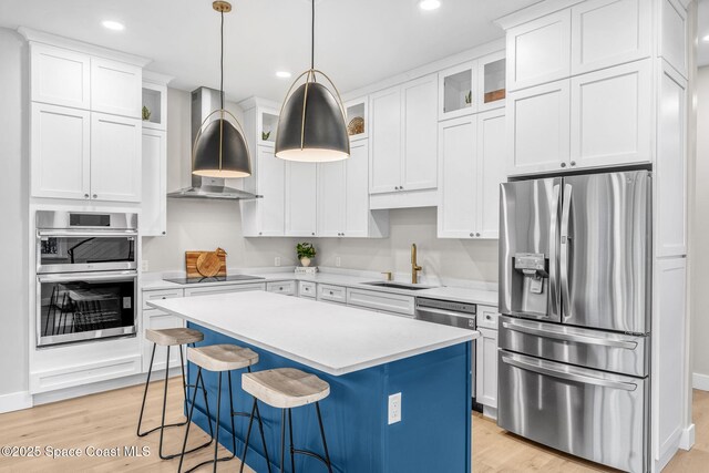 kitchen featuring appliances with stainless steel finishes, pendant lighting, a kitchen island, wall chimney exhaust hood, and sink