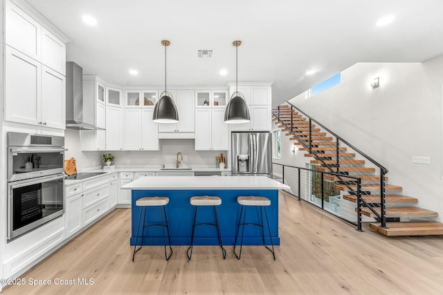 kitchen with wall chimney range hood, pendant lighting, a kitchen island, white cabinetry, and appliances with stainless steel finishes