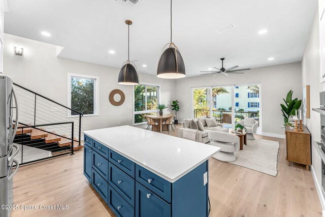 kitchen with pendant lighting, a center island, blue cabinetry, light wood-type flooring, and ceiling fan