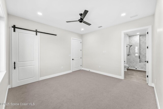 unfurnished bedroom with ceiling fan, light colored carpet, connected bathroom, and a barn door