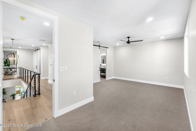 unfurnished living room featuring ceiling fan with notable chandelier, carpet flooring, and a barn door