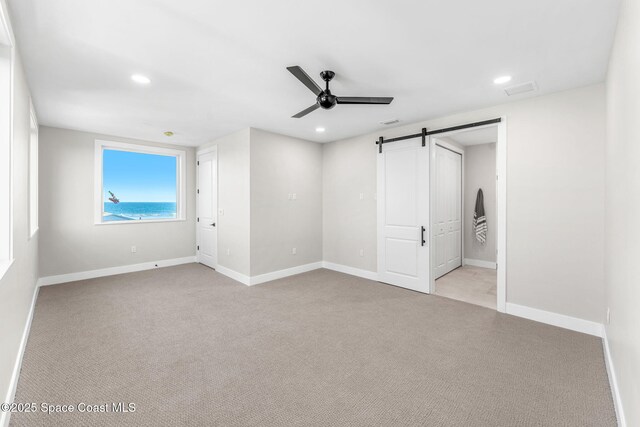 unfurnished bedroom featuring ceiling fan, light colored carpet, and a barn door