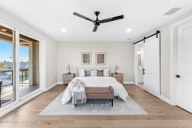 bedroom featuring access to outside, light wood-type flooring, ceiling fan, ensuite bathroom, and a barn door