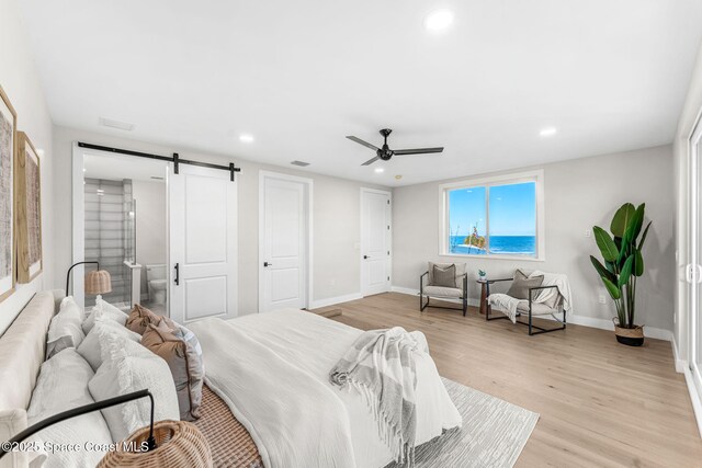 bedroom with ceiling fan, a barn door, and light hardwood / wood-style flooring