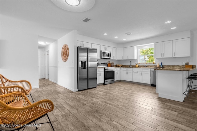 kitchen with kitchen peninsula, white cabinetry, stainless steel appliances, and light wood-type flooring