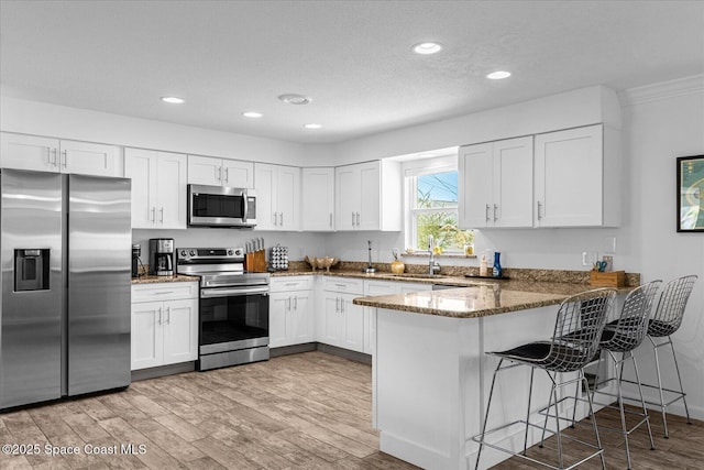 kitchen featuring sink, stainless steel appliances, kitchen peninsula, dark stone countertops, and white cabinets