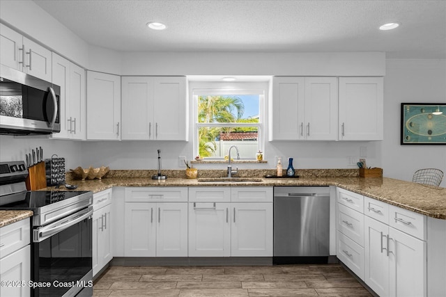 kitchen featuring stone counters, appliances with stainless steel finishes, white cabinetry, and sink