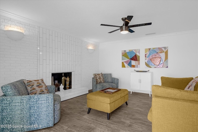 living room with brick wall, ceiling fan, crown molding, hardwood / wood-style flooring, and a fireplace