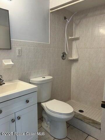 bathroom with tile patterned floors, vanity, a tile shower, and tile walls