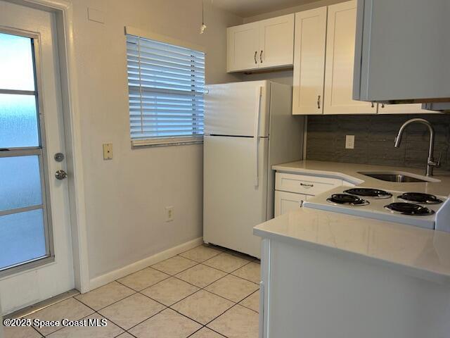 kitchen featuring white cabinetry, sink, backsplash, white fridge, and light tile patterned flooring