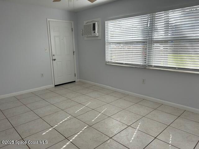 tiled empty room with ceiling fan and a wall unit AC