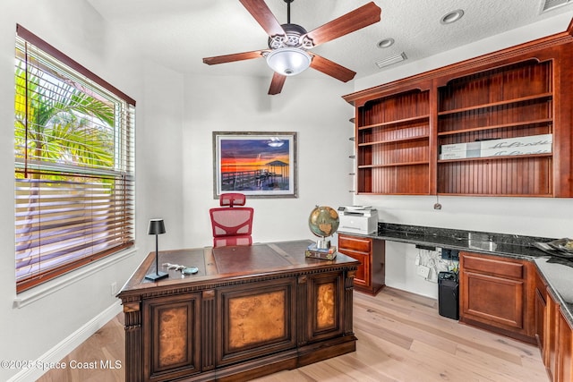 office space with ceiling fan, built in desk, a textured ceiling, and light wood-type flooring