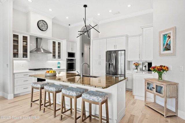 kitchen featuring dark stone countertops, white cabinets, wall chimney range hood, stainless steel appliances, and a center island with sink