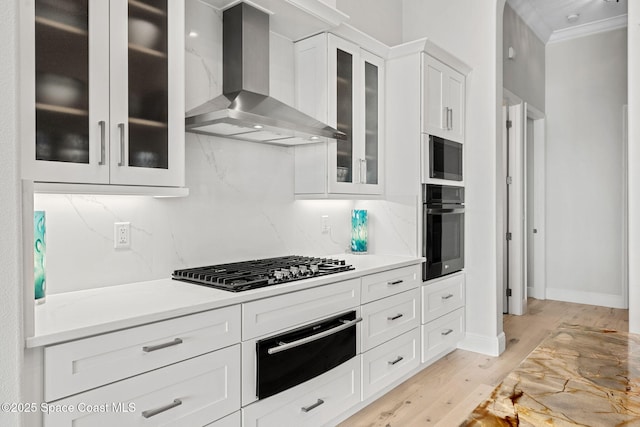 kitchen with stainless steel gas cooktop, black oven, wall chimney range hood, light hardwood / wood-style floors, and white cabinets