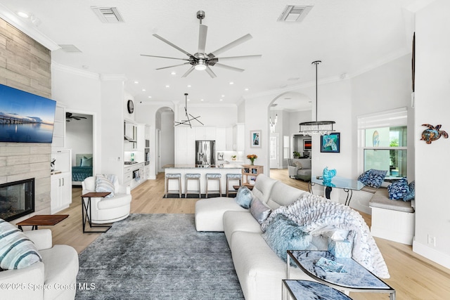 living room with crown molding, a large fireplace, and ceiling fan with notable chandelier