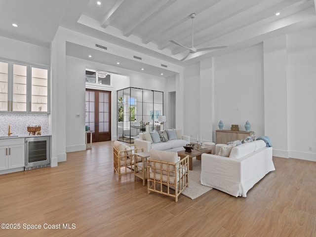 living room with wet bar, beam ceiling, ceiling fan, wine cooler, and light wood-style floors