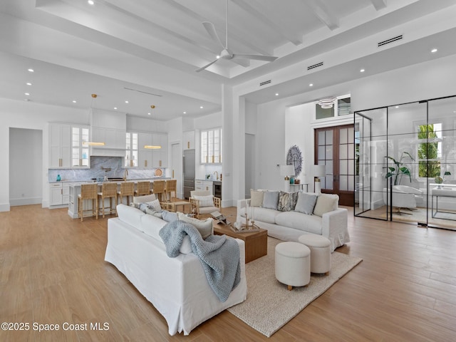 living room with visible vents, beam ceiling, light wood-style flooring, and a ceiling fan