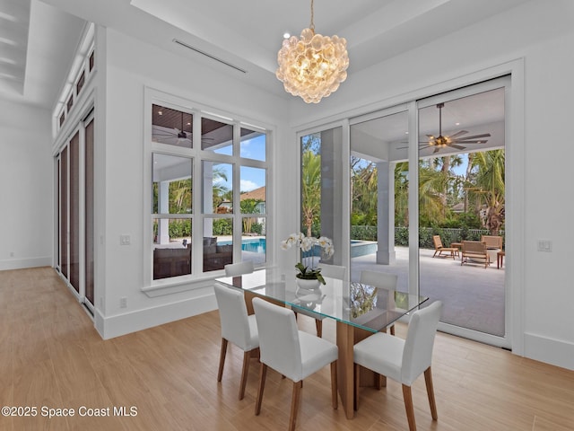 dining space with light wood-style flooring, ceiling fan with notable chandelier, and baseboards