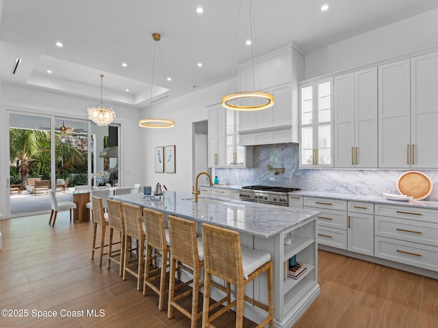 kitchen with range with gas cooktop, a breakfast bar area, light wood finished floors, decorative backsplash, and a raised ceiling