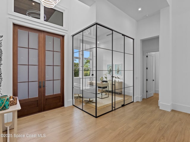 doorway to outside featuring light wood-type flooring, french doors, baseboards, and a towering ceiling