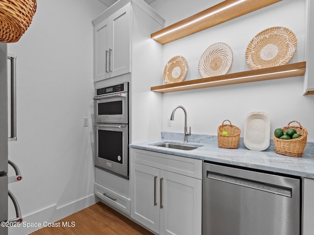 kitchen with appliances with stainless steel finishes, light stone countertops, open shelves, and a sink