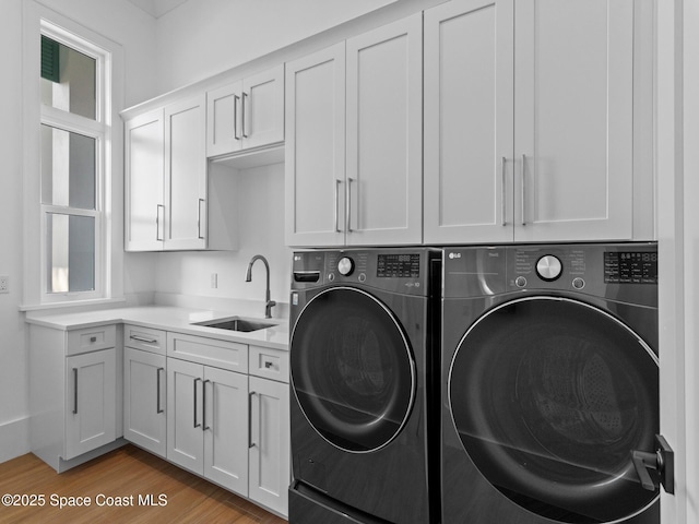 clothes washing area with cabinet space, wood finished floors, separate washer and dryer, and a sink