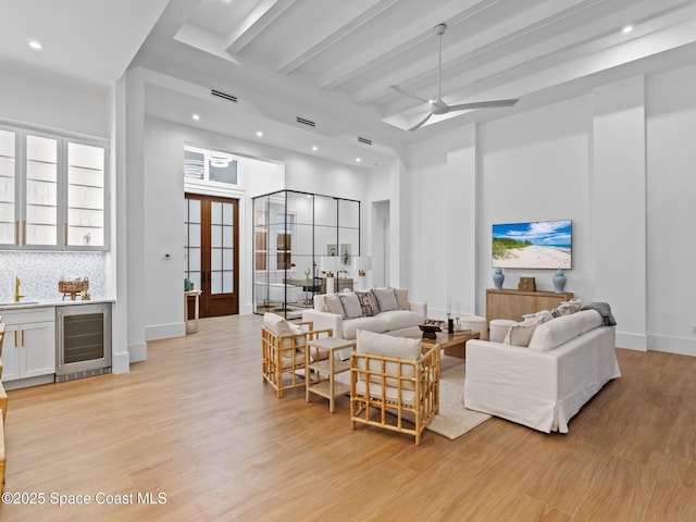 living area with beverage cooler, beam ceiling, indoor wet bar, and light wood-type flooring