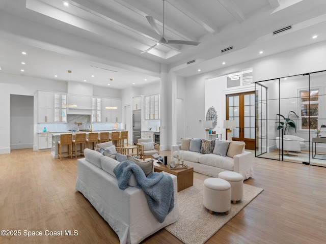 living area featuring beamed ceiling, light wood-style floors, visible vents, and a ceiling fan