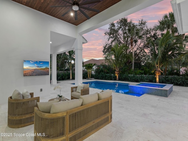 pool at dusk featuring a ceiling fan, a pool with connected hot tub, a patio, fence, and an outdoor hangout area