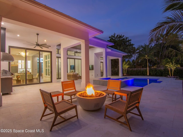 patio terrace at dusk featuring an outdoor fire pit, a ceiling fan, a fenced in pool, and an outdoor kitchen