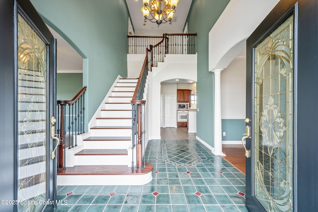 tiled entrance foyer with a towering ceiling, ornate columns, and a notable chandelier